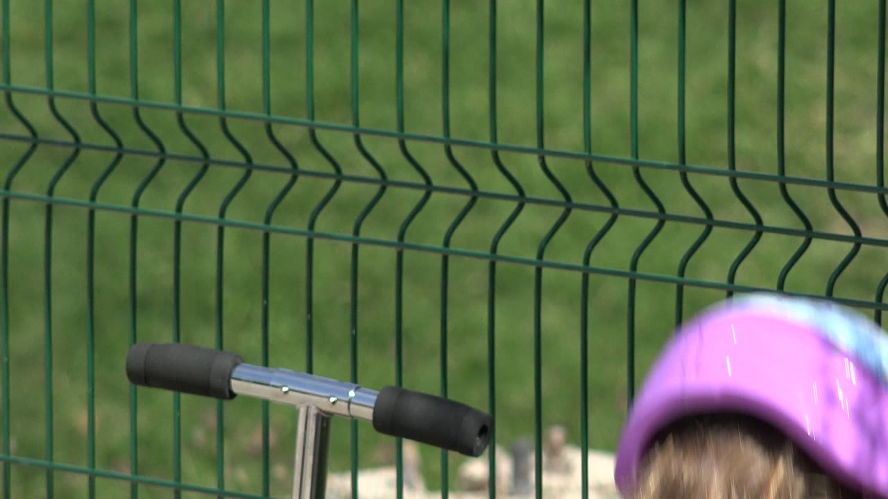 Purple helmet and scooter handlebar in front of a green fence