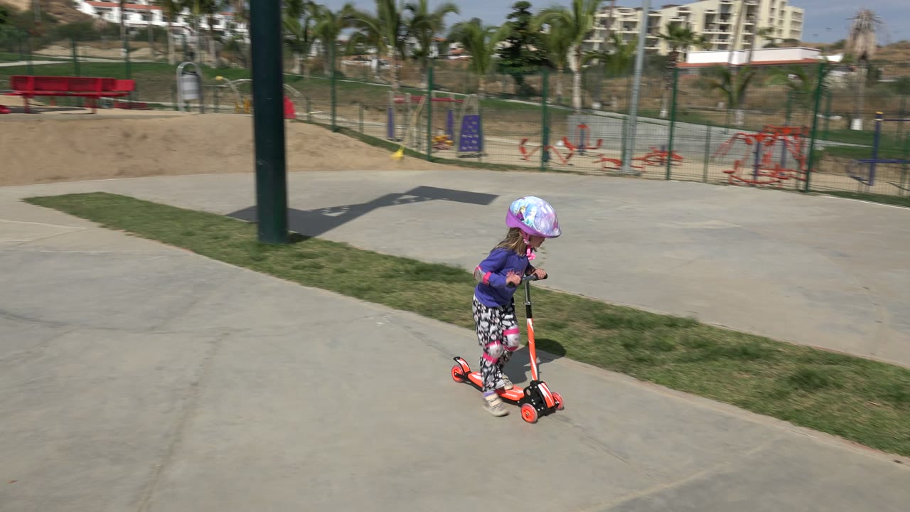 Young child in a helmet riding a scooter on a park path.