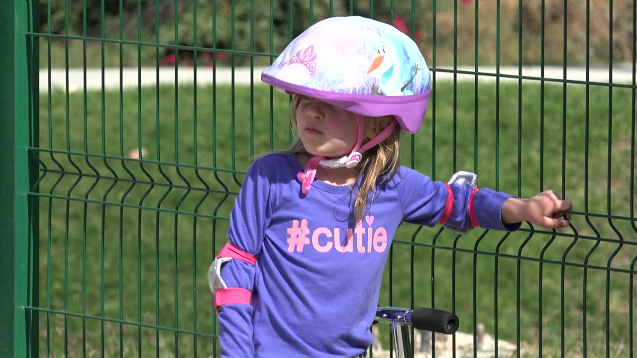 Young child in a purple helmet and shirt beside a green fence.