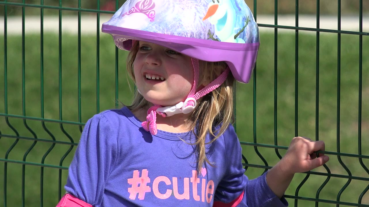 Girl in purple shirt and helmet looking to the side by a fence.