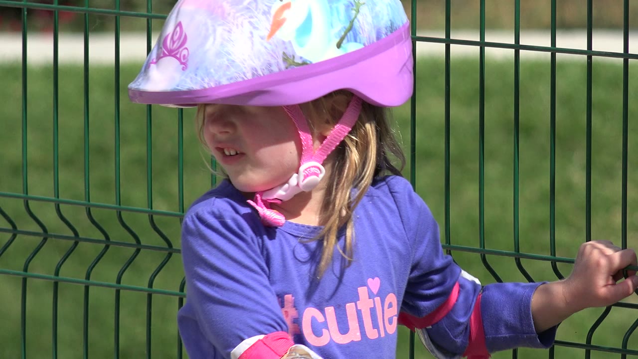 Young girl in purple helmet beside a green fence.