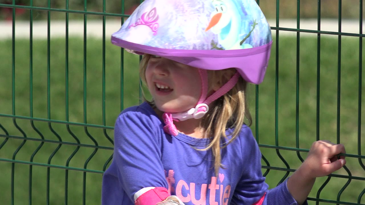 The child smiles under a purple helmet while holding one hand near the green fence in Los Cabos, Mexico.