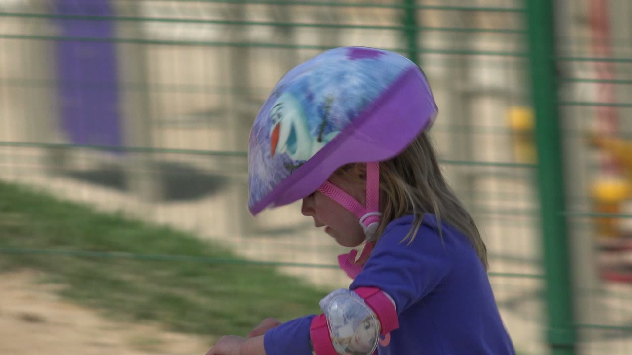 Helmeted girl riding with park chairs behind a fence.