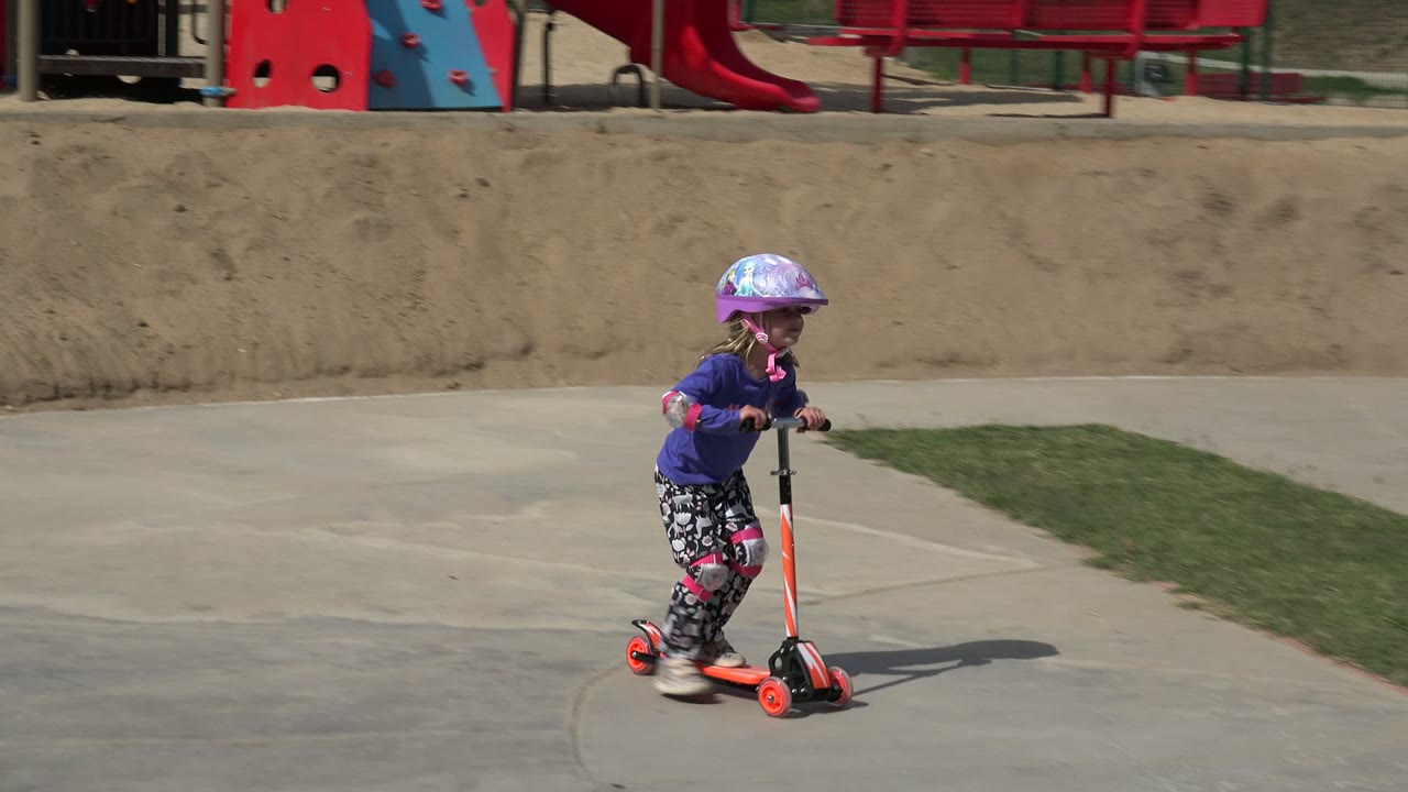 Young girl riding an orange scooter on a paved path.