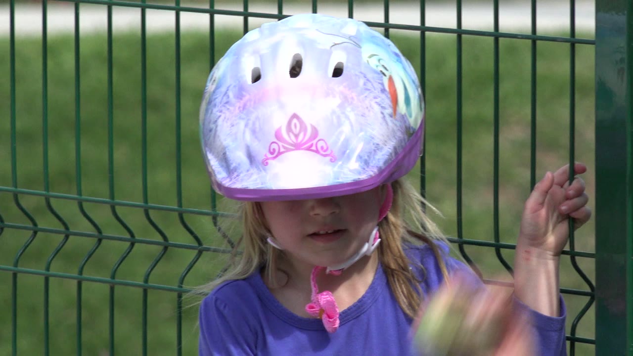 Young girl in a purple helmet and shirt beside a green fence.