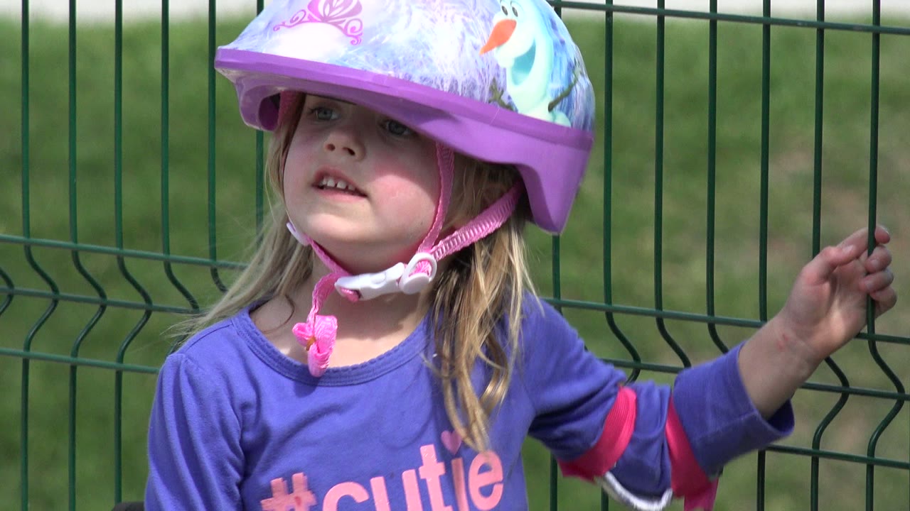 Young girl in Los Cabos, Mexico looks upward from under a purple illustrated helmet while one hand rests near the green fence.