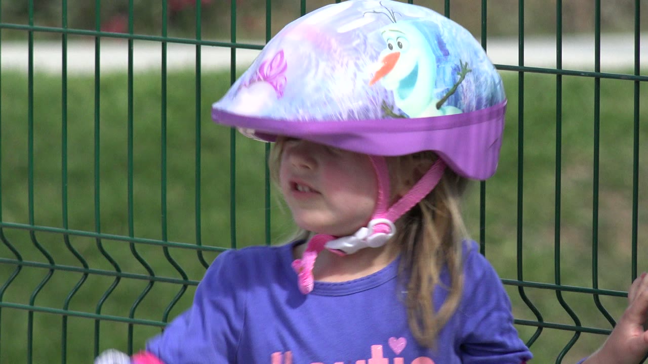 Girl turned slightly sideways in a large helmet near a fence.