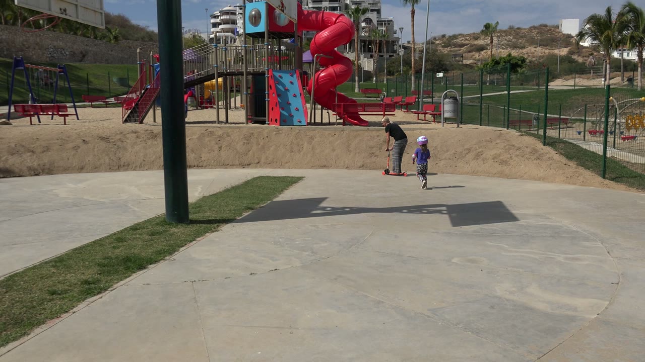 Father and child with scooter near a playground slide.