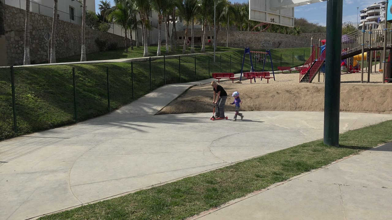 Young girl and adult with a scooter near a skate park path.