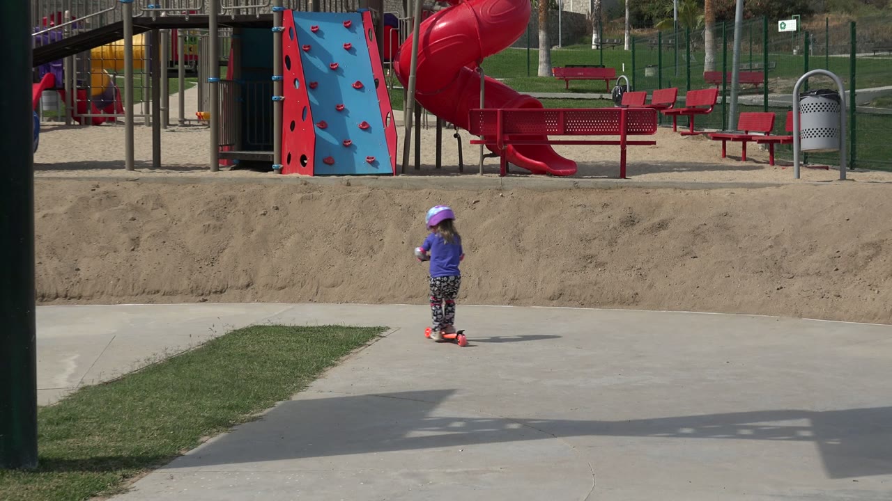 Helmeted child on a scooter near playground equipment.