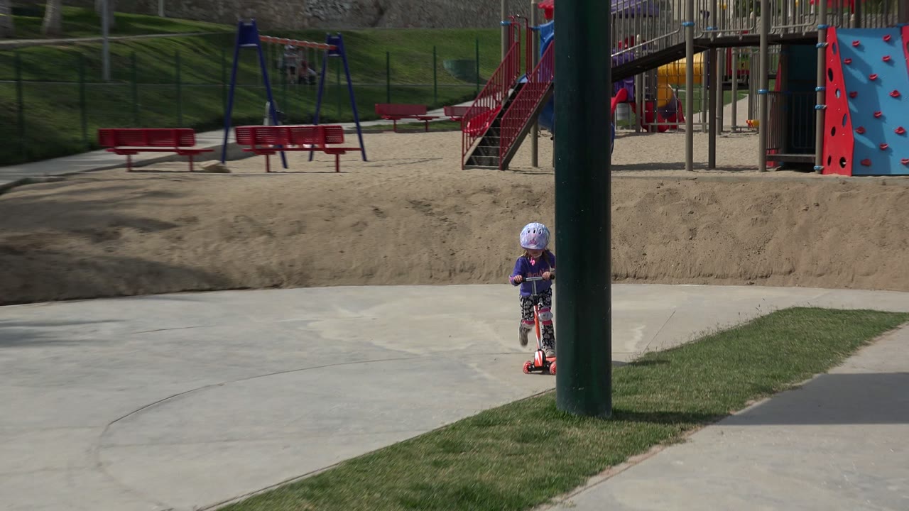 Small child on a red scooter near playground equipment.
