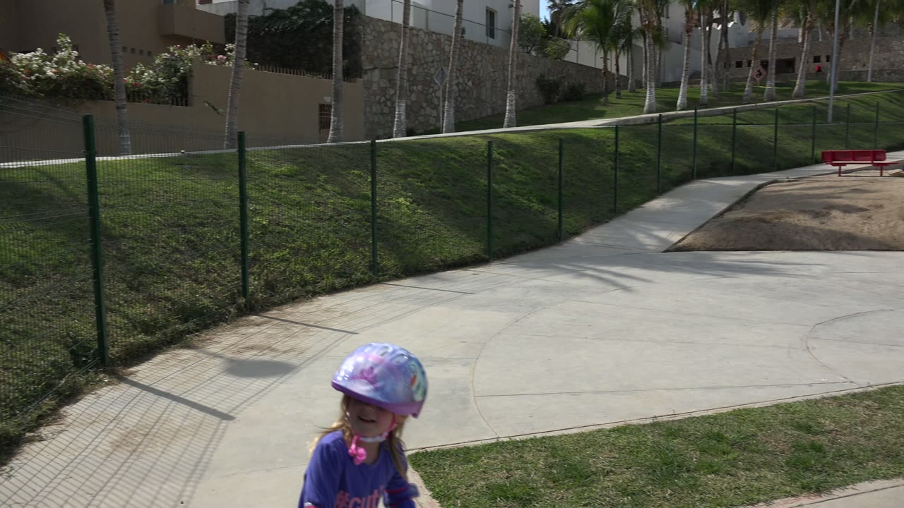 Young girl in a purple helmet entering the lower edge of a paved park path.