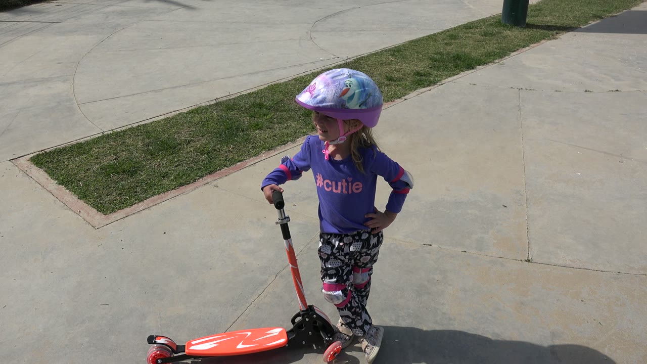Young girl standing beside a red scooter on concrete.