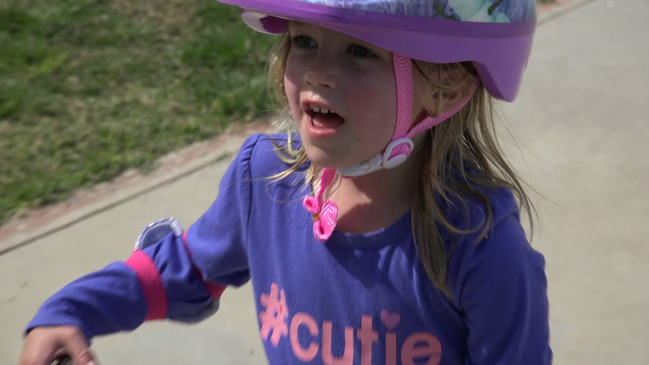 A closer frame shows the young girl in Los Cabos, Mexico wearing a purple helmet, with her face partly shaded by the helmet brim and grass behind her.
