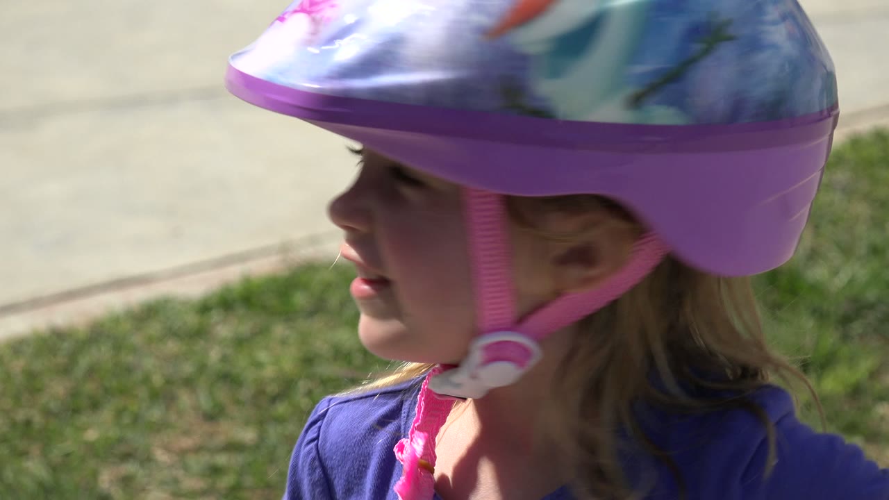 Helmeted blonde child shown in side profile outdoors.