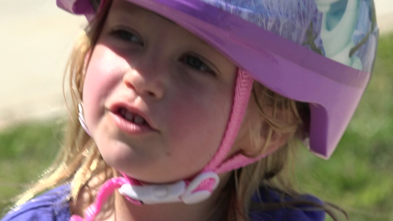 Close-up of a young girl in a purple helmet outdoors.