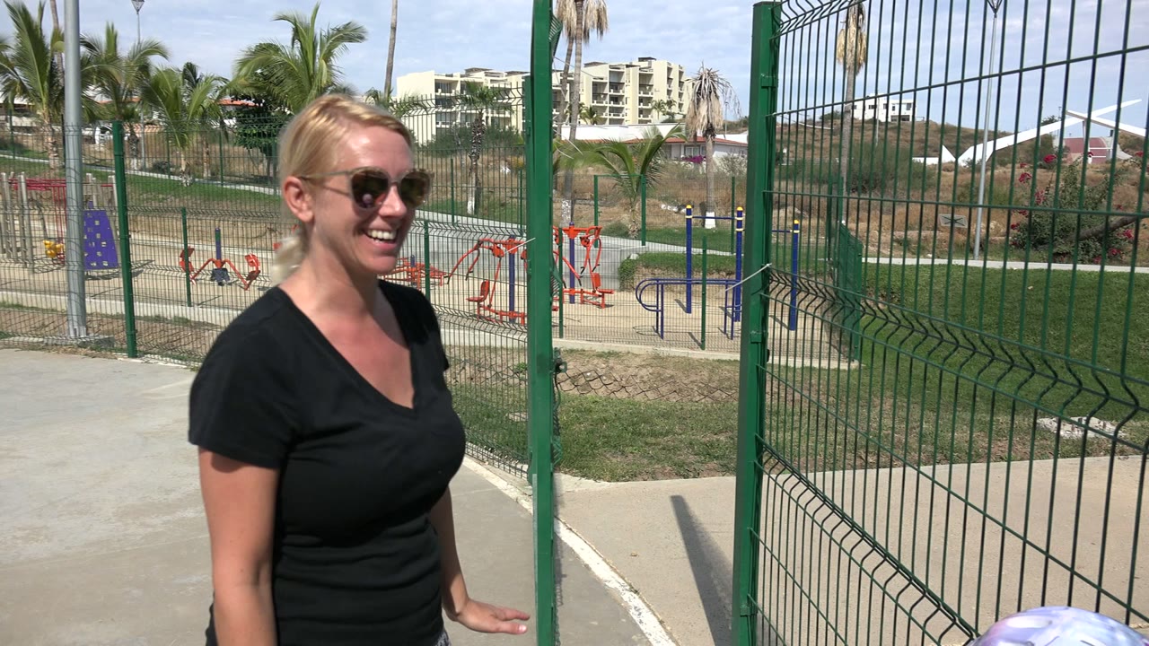 The smiling woman faces the camera beside the green fence in Los Cabos, while the top of a child's colorful helmet enters the lower foreground.