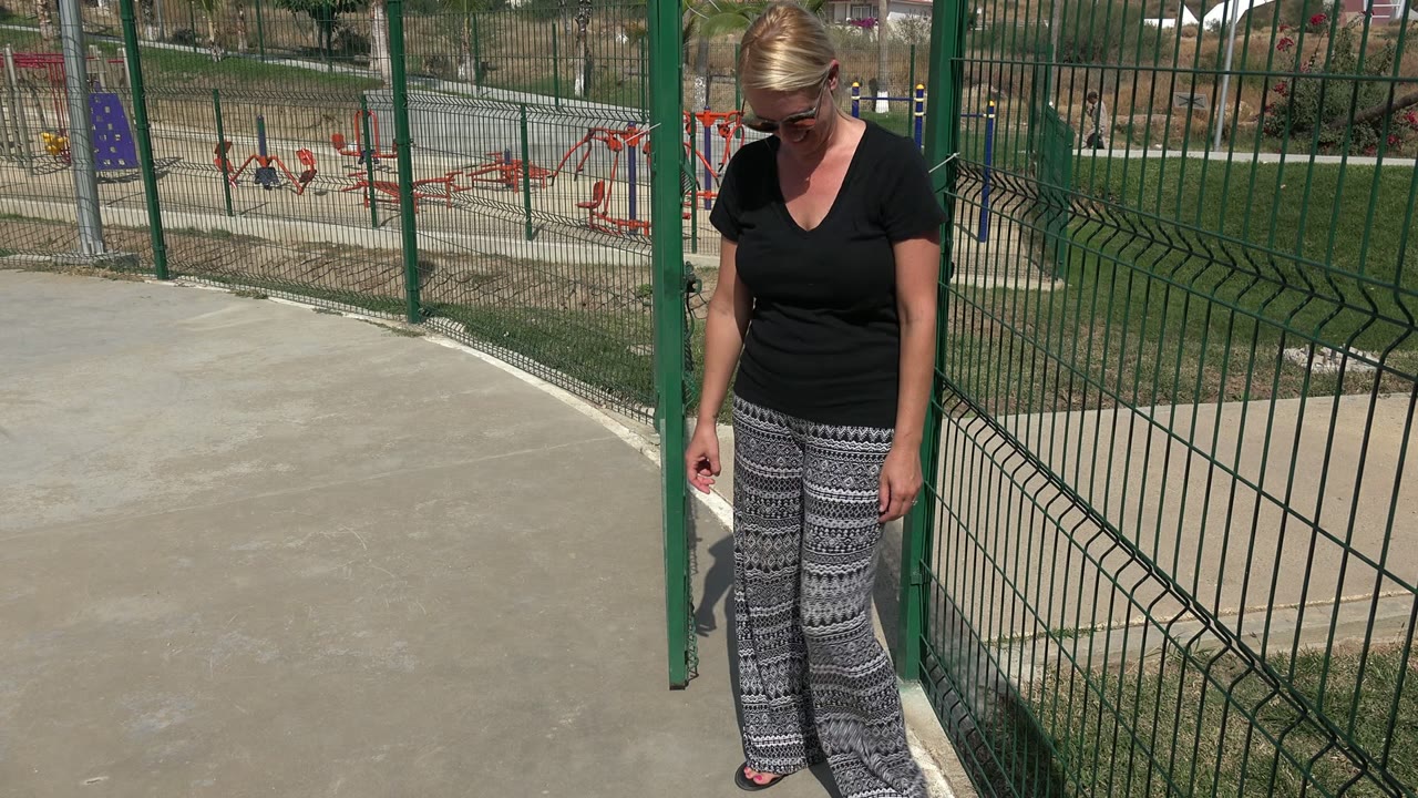 Woman standing by a green fence at an outdoor playground.