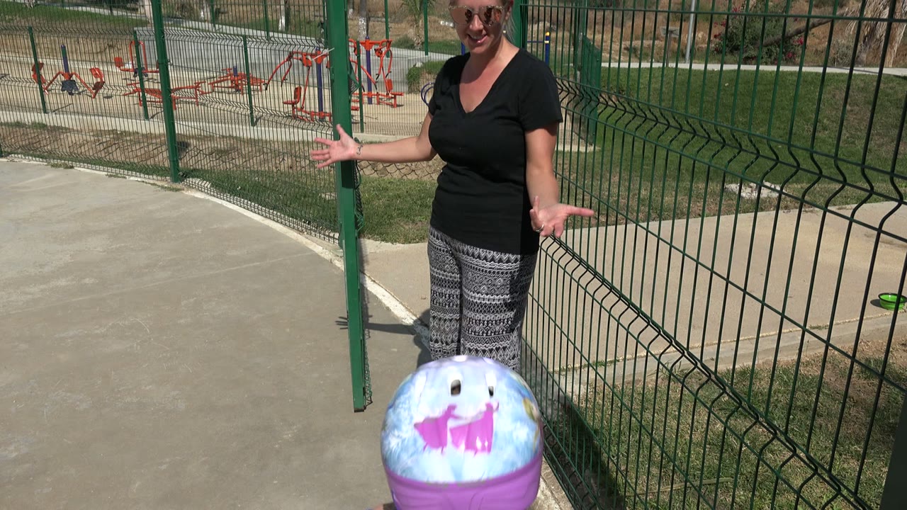 At 0:01 in Los Cabos, the woman stands near the green fence with her arms open as the girl's purple helmet appears in the foreground.