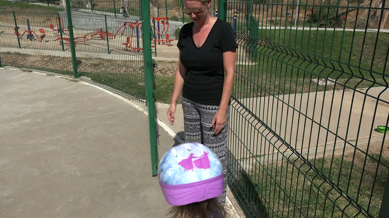 Woman looks down toward a young girl in a purple helmet at the playground.