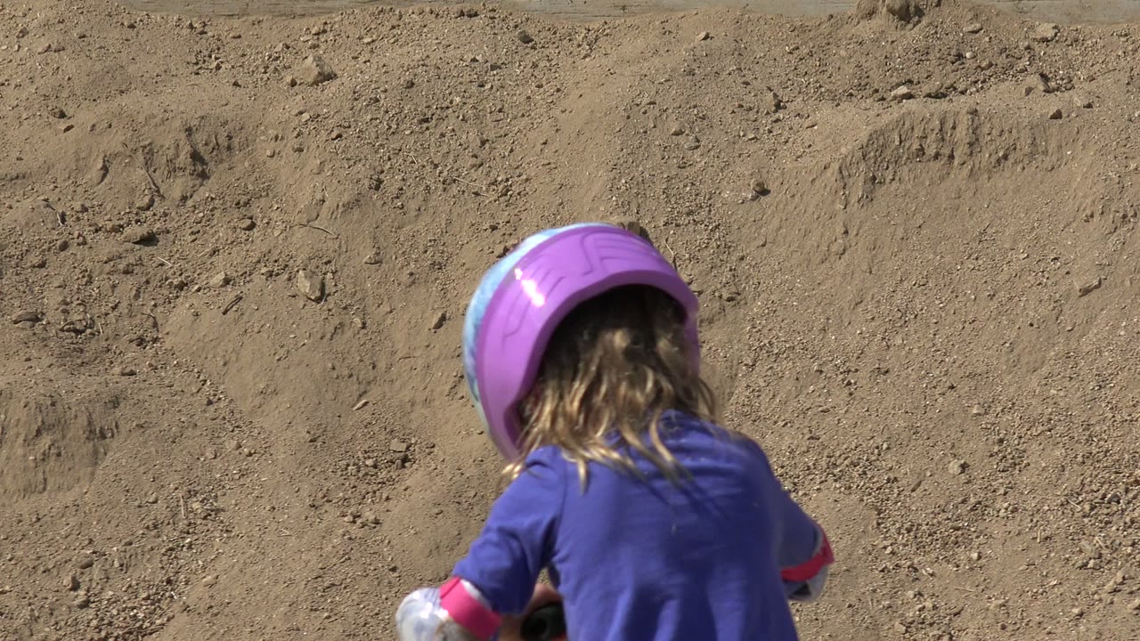 The child is partially visible below the center of frame in Los Cabos, Mexico, with a purple helmet and hair showing against the textured sand bank.