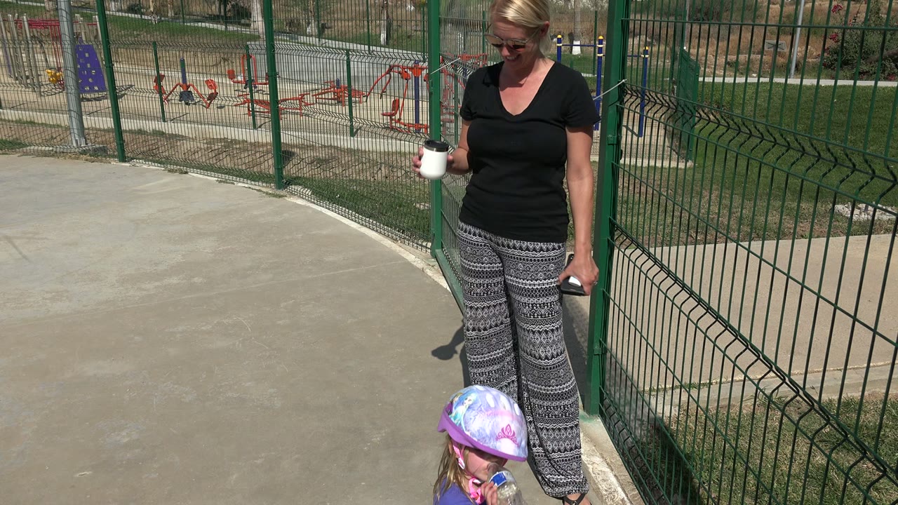Woman looking down near a child in a helmet by the fence.