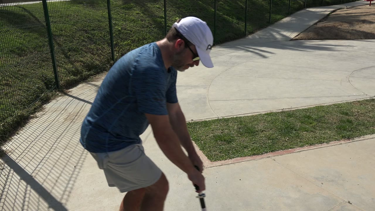 Man in a white cap leaning over a red scooter on a concrete park path.