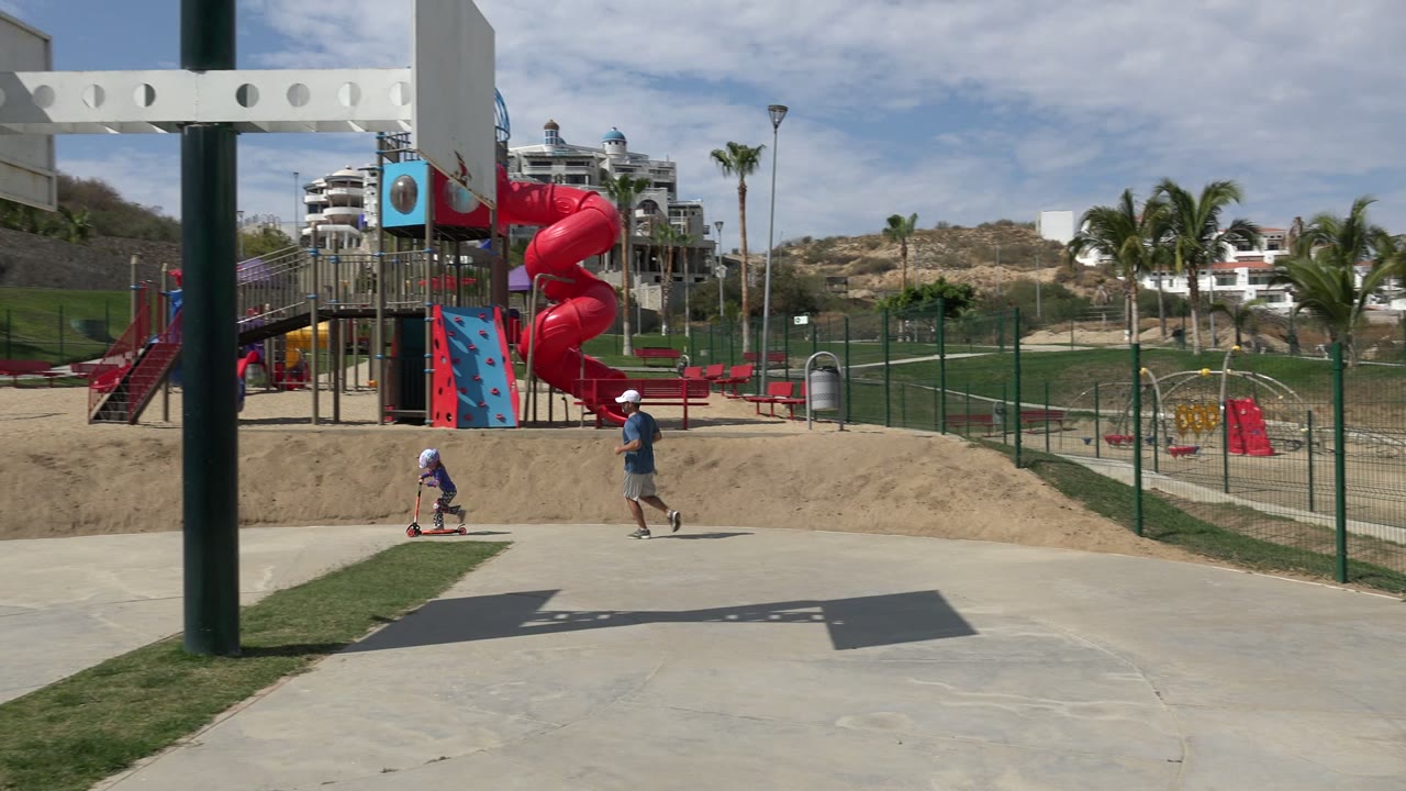 Child on a scooter and man running in a sunny playground park.
