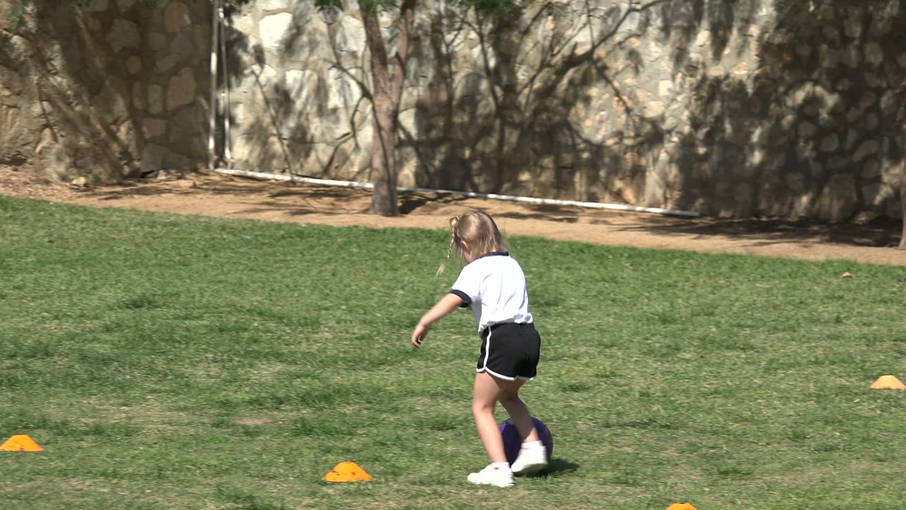 Young girl dribbling a soccer ball near orange cones on a grass field.