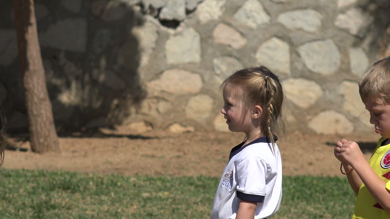 In Los Cabos, Mexico, the blonde girl faces left while the boy in the yellow jersey looks down at his hands beside her on the grass.