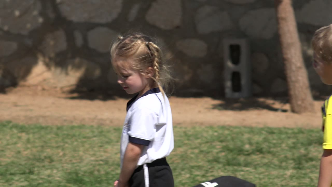 Young girl in a white soccer shirt standing on a grass field.