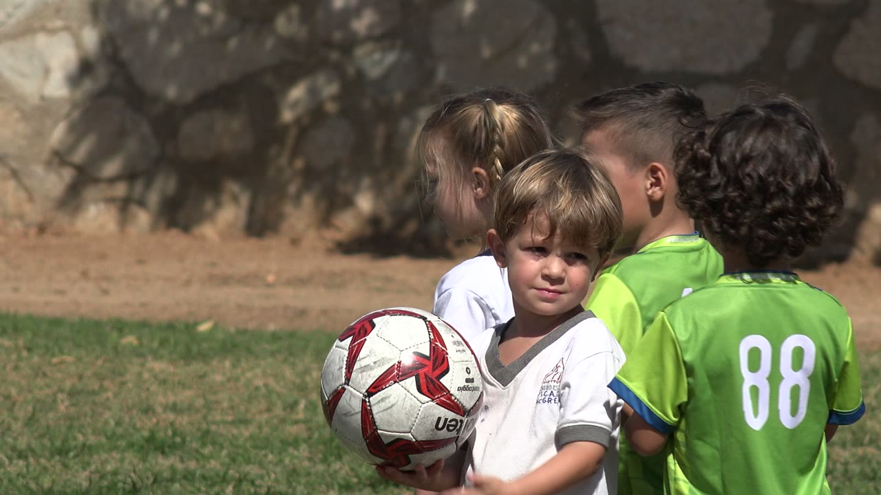 One second in, several young soccer players cluster on the Los Cabos field, with a blond boy facing the camera and green jersey numbers visible from behind.