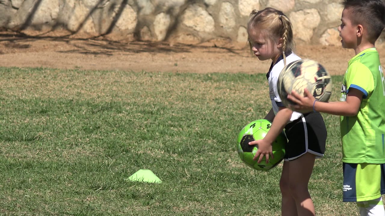 Two children holding soccer balls on a grass field