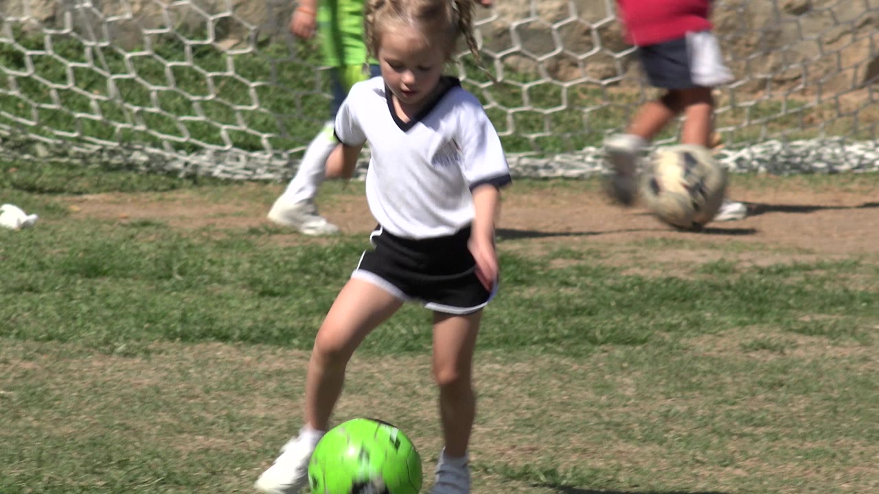 Young blond girl near a bright green soccer ball on a grass field.