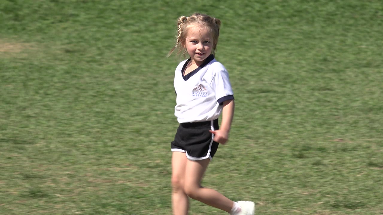 Young girl walking across a grass soccer field.
