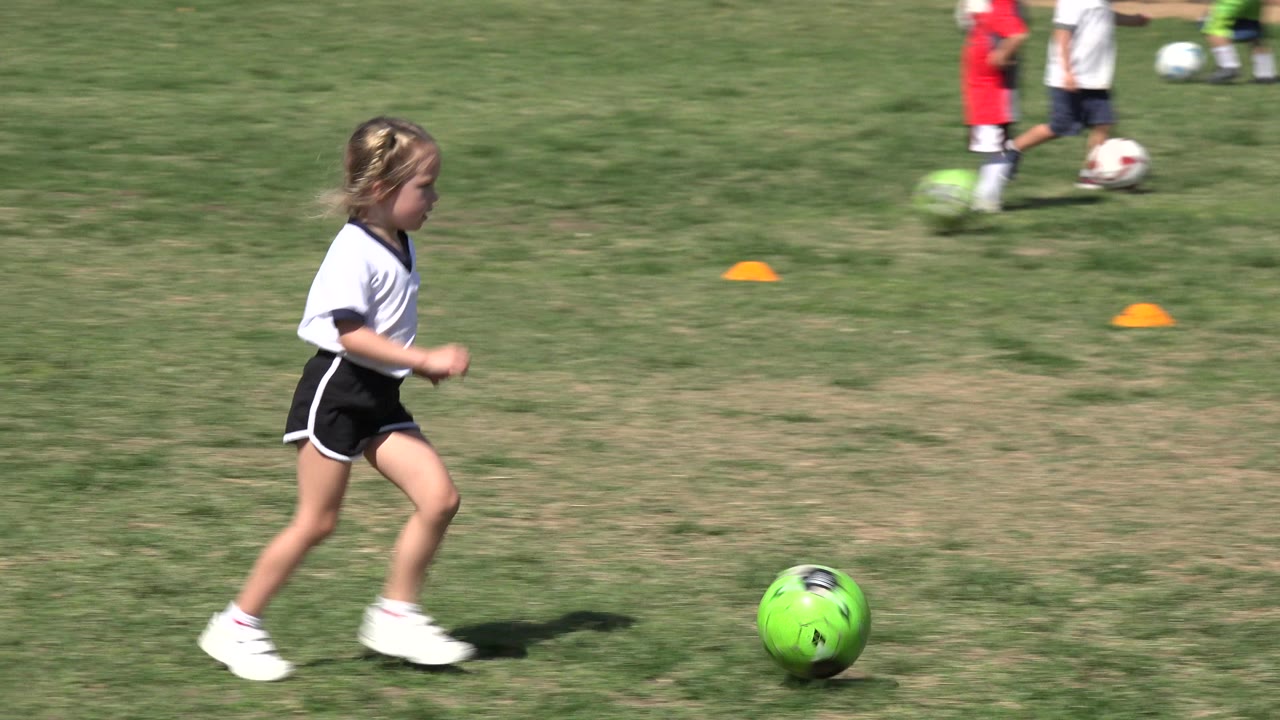 Young child running toward a green soccer ball on a grass field.