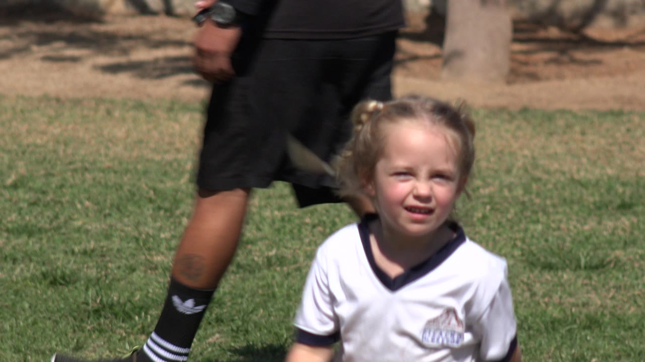 Young girl on a soccer field with an adult walking behind her.