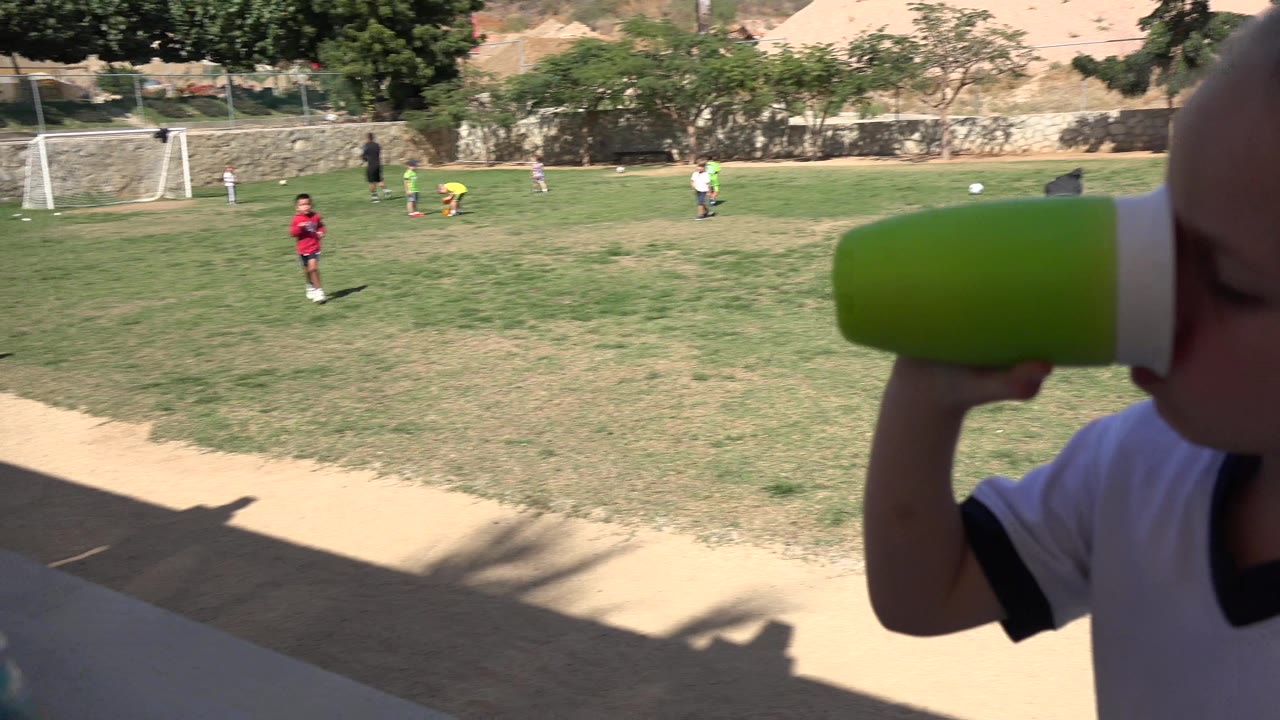 Young girl drinking from a green cup beside a soccer field.
