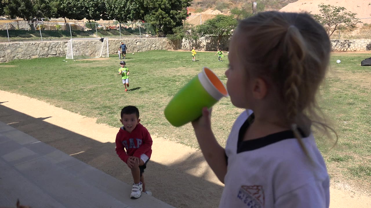 Child drinking from a green cup beside a grassy football field.