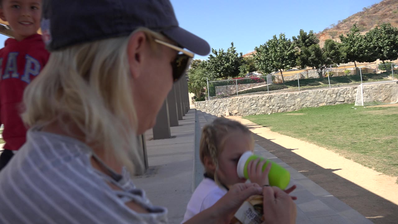 Woman in cap beside children at a shaded park walkway.