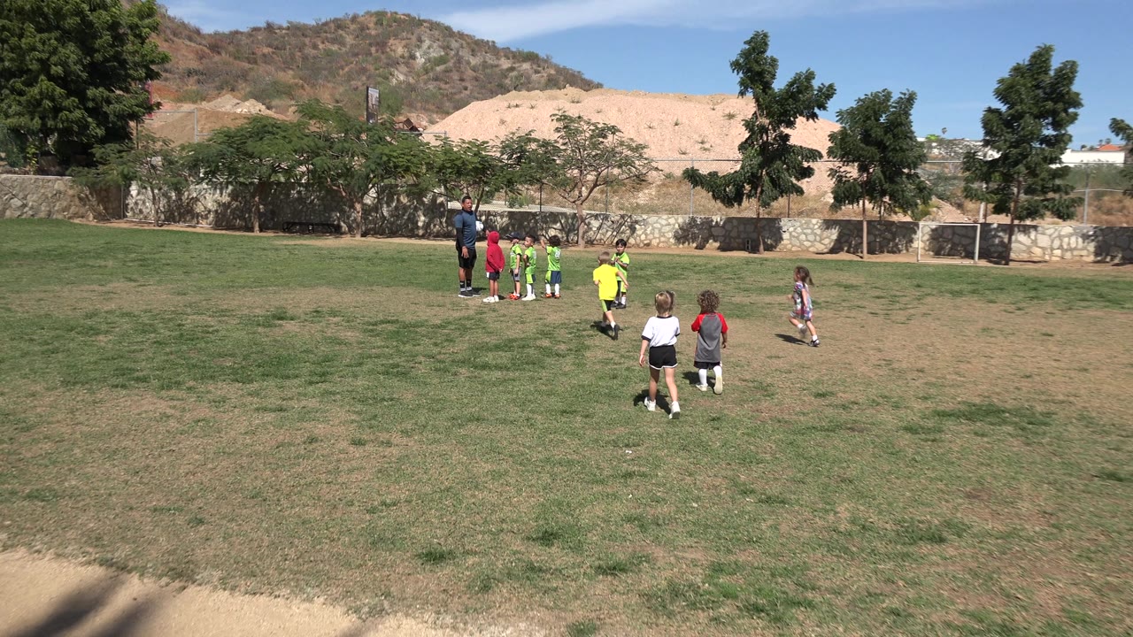 Kids gather near a coach on a sunny grass field.