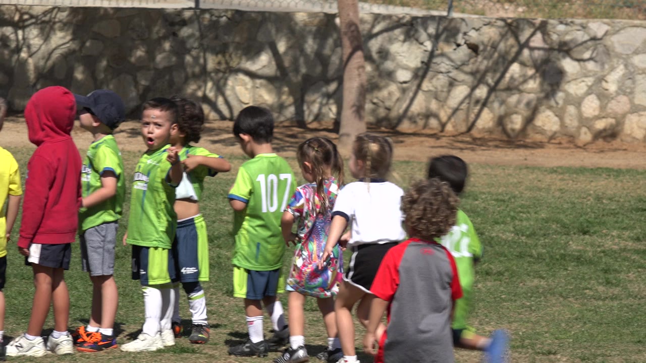 Children in green soccer uniforms gather on a grassy field.