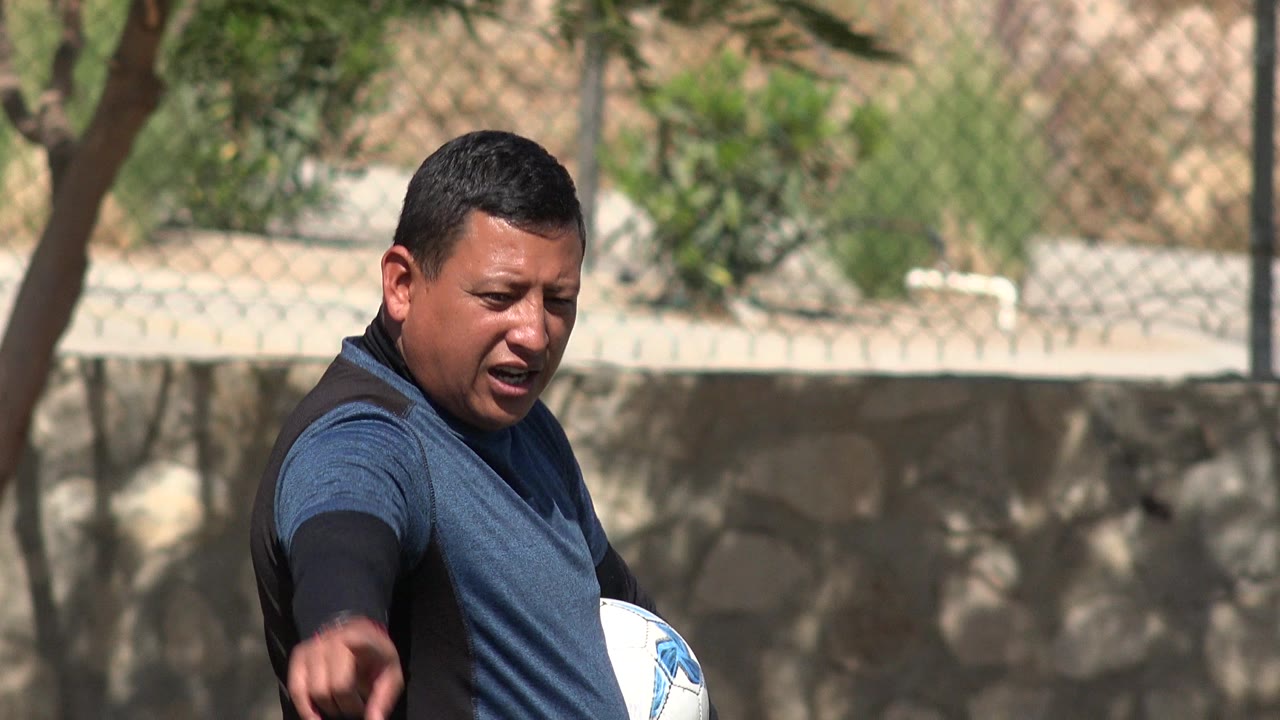 Man holding a soccer ball and pointing on a field.
