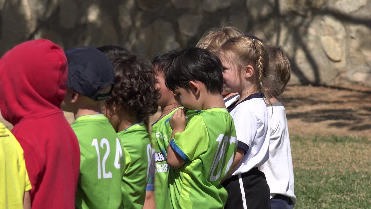 Children in green and white sports shirts standing in a line outdoors.