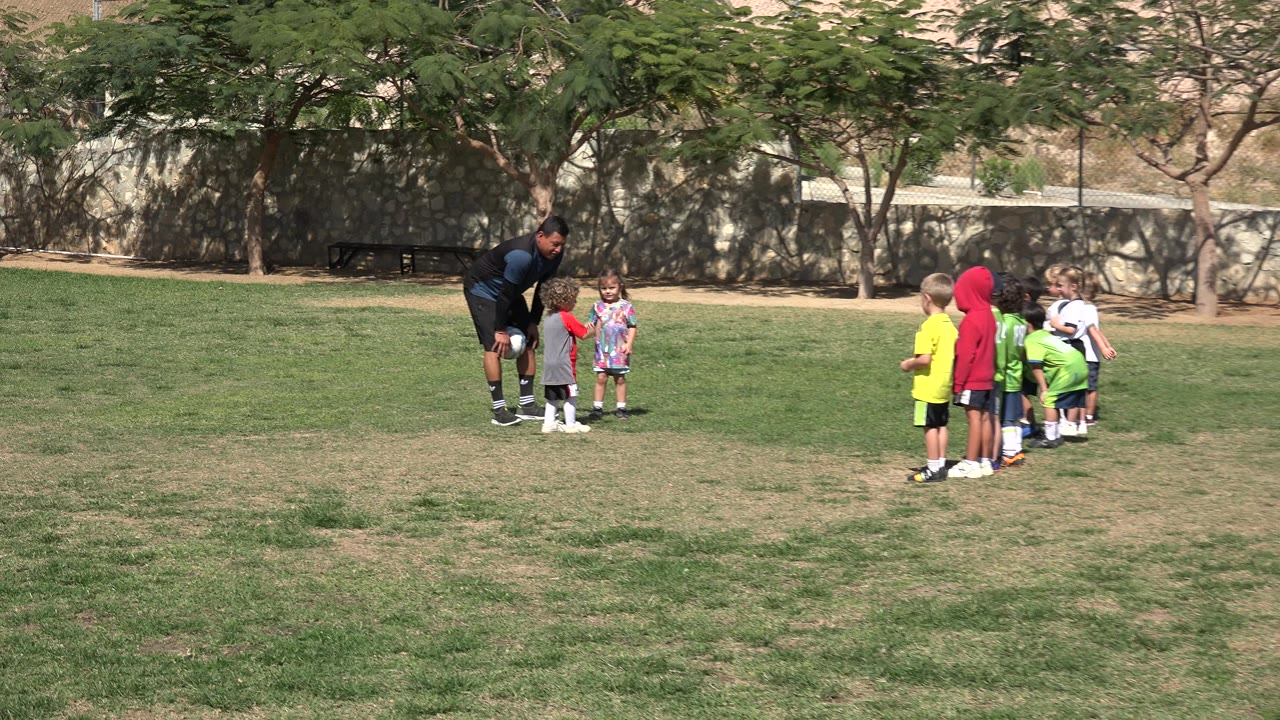 Adult bends toward children on a grass field.