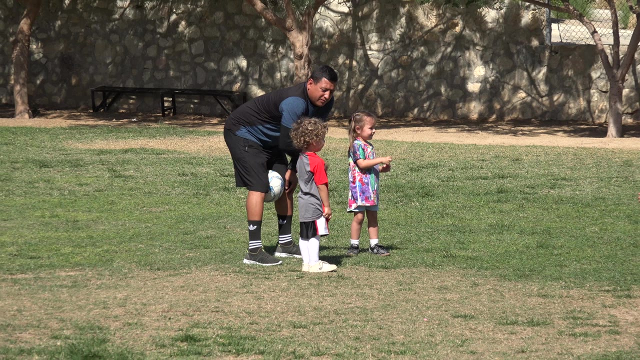 Adult crouching beside two children on a grass field.
