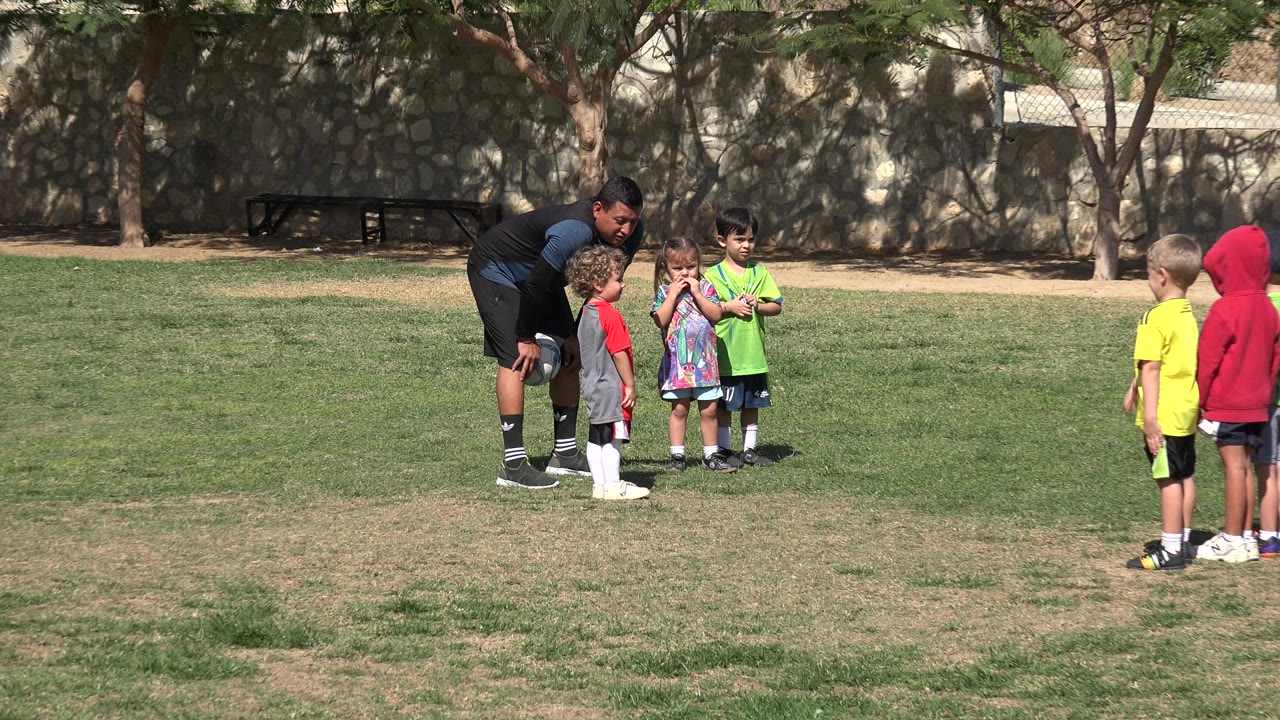 Coach crouching near young children on a grass soccer field.