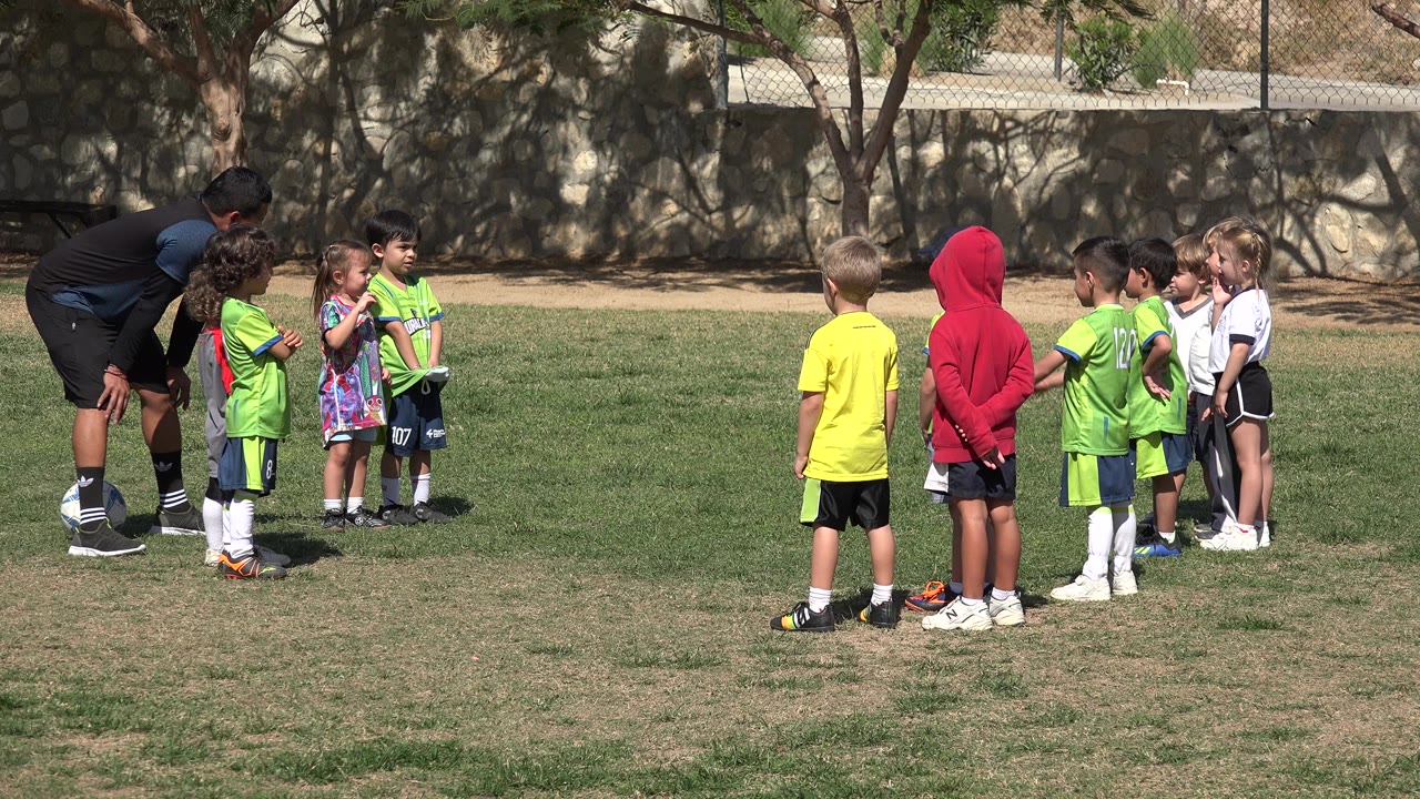Coach bends toward children gathered on a grassy field.