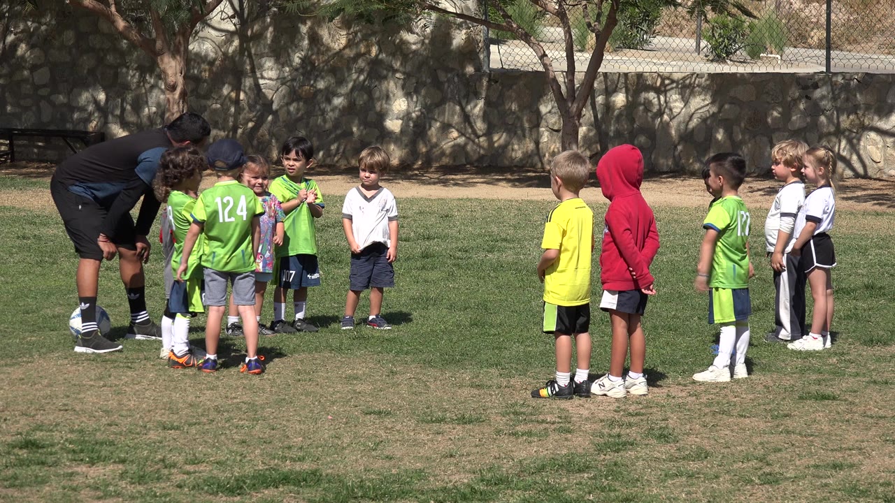 Coach bends toward children gathered on a soccer field.