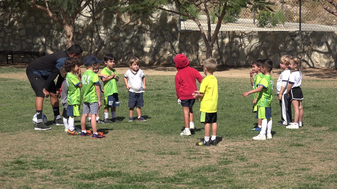 Coach speaking to children on a grass field.